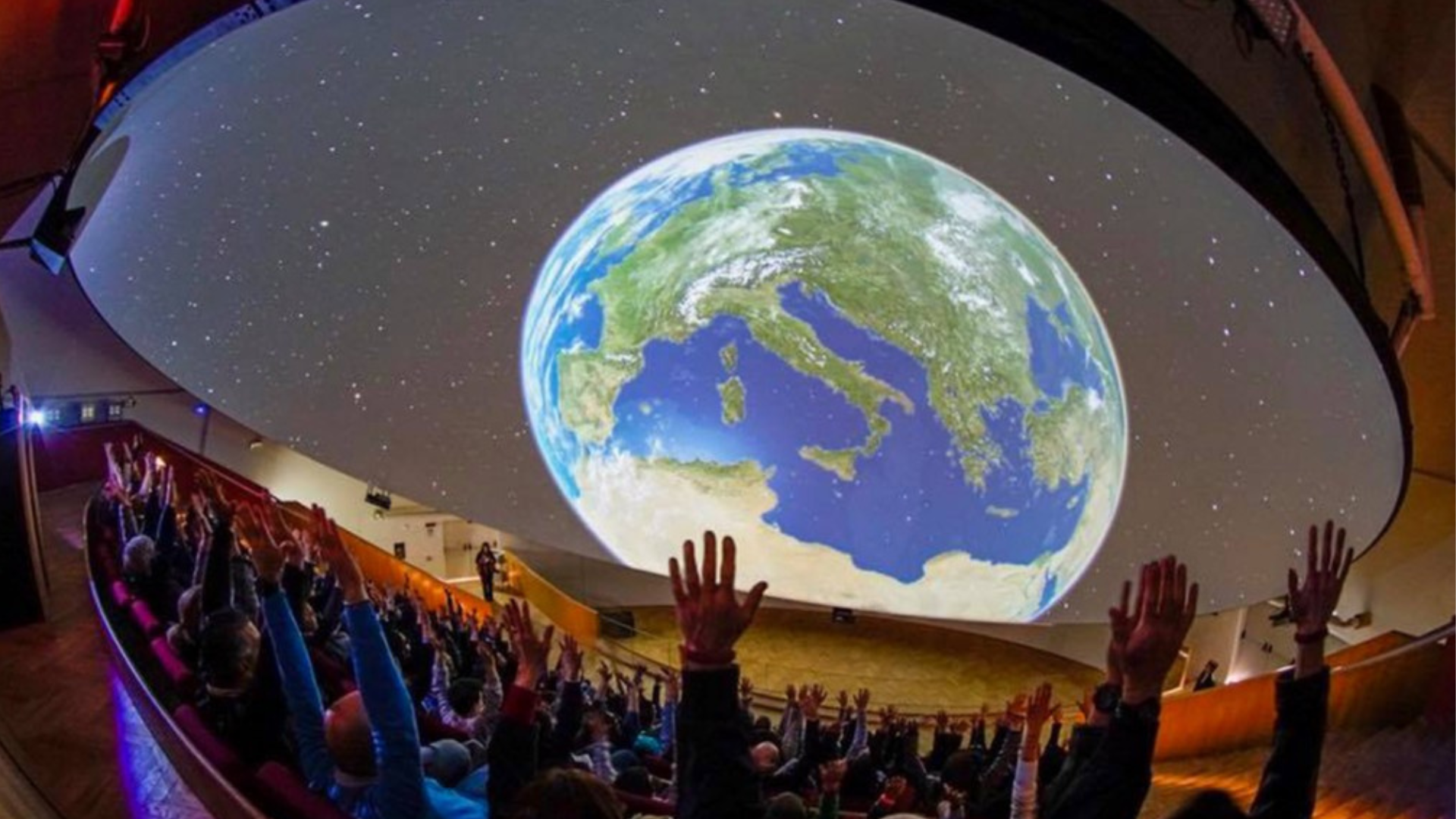 mani e teste di pubblico che assistono allo spèettacolo del planetario a ciità della scienza di Napoli, imagine della terra dal cosmo